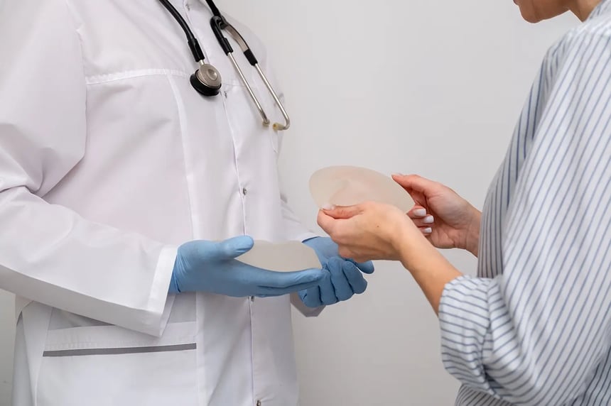 A doctor shows a patient a breast implant during a consultation to help distinguish volume loss from sagging when considering a breast lift in Singapore