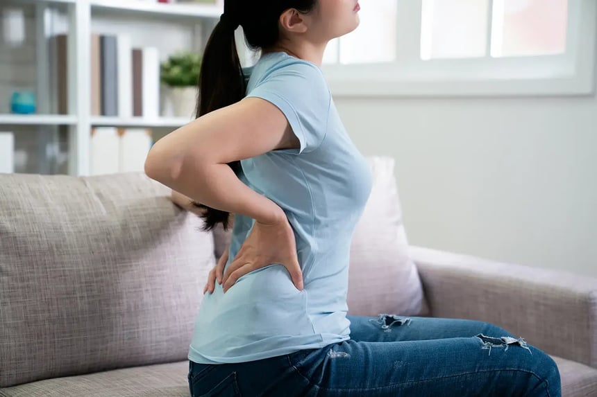 A woman holds her lower back while experiencing pain caused by large breasts.
