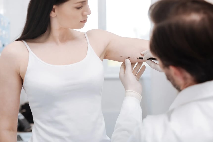 A plastic surgeon assessing a woman’s arm during a consultation for liposuction.